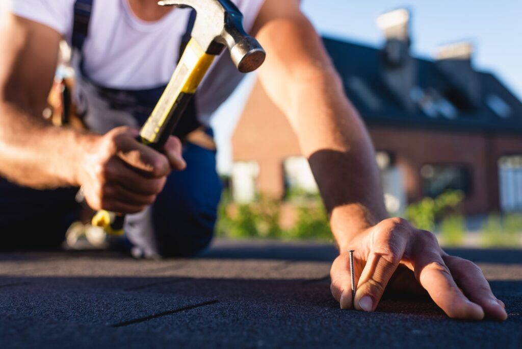 Cropped view of builder holding hummer and nail while repairing roof of building